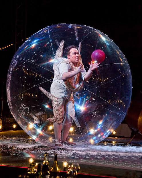 Artiste costumé tenant un ballon rouge à l’intérieur d’une bulle de déambulation transparente