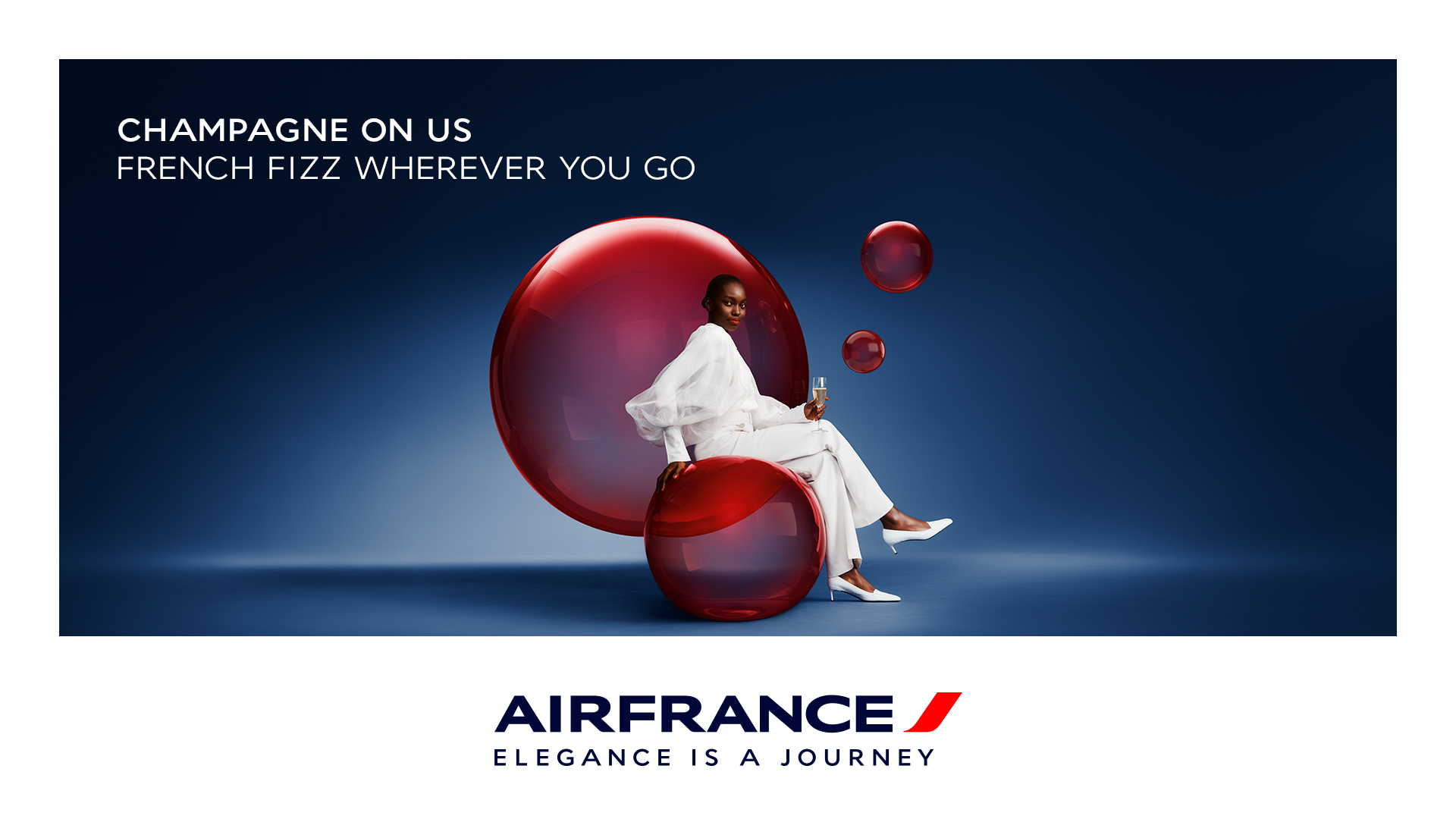Visuel Air France avec une femme en blanc assise devant de grandes bulles rouges sur fond bleu