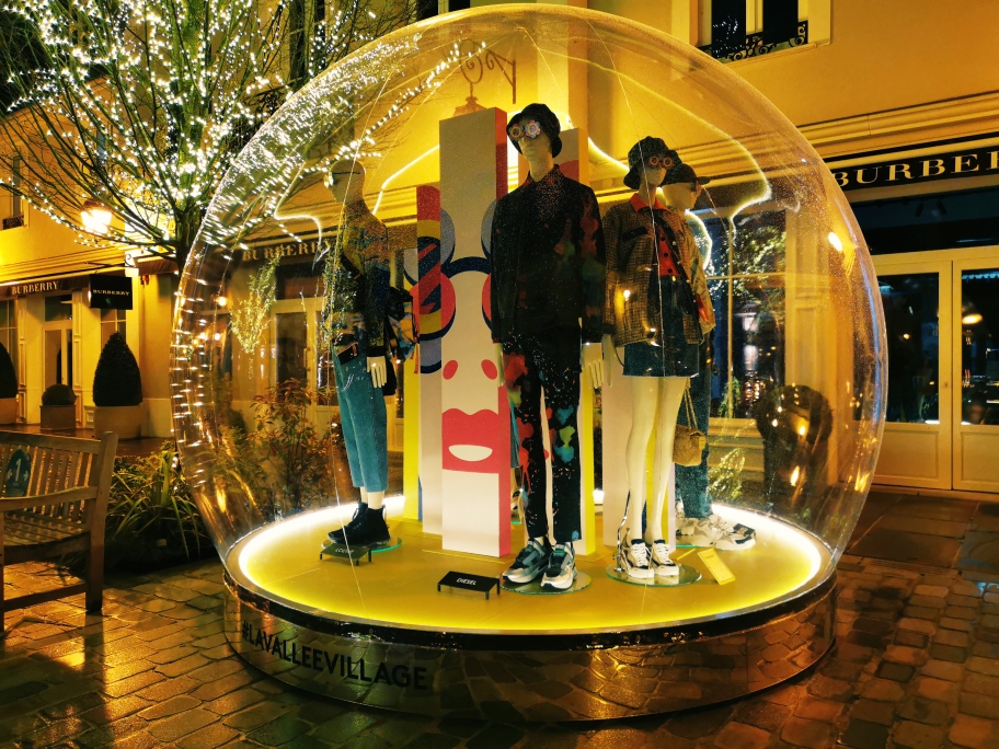 Vitribulle illuminée présentant des mannequins à La Vallée Village de nuit